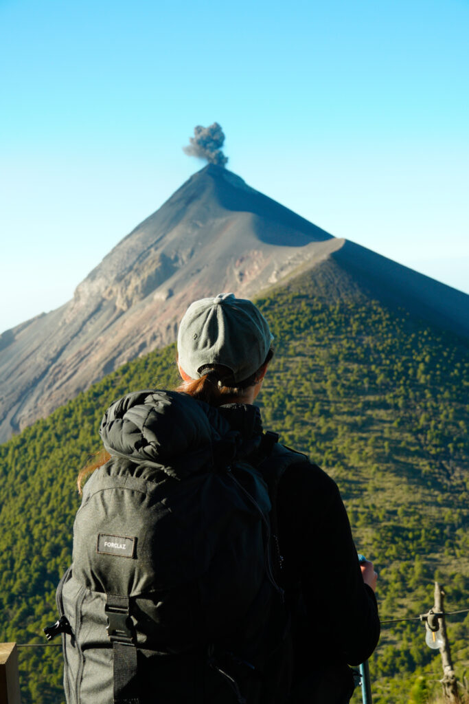 A man wearing a hat and a backpack is standing on a mountain.