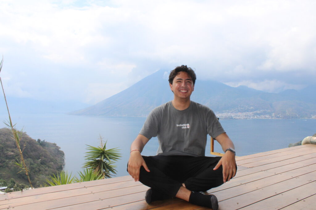 A man wearing a black shirt and black pants is sitting on a wooden deck.